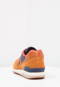 Oranžové semišové tenisky s námořnickými akcenty, zaoblený tvar, polstrovaný límec, texturovaná pata a detail značky na boku. Bílé podešev.