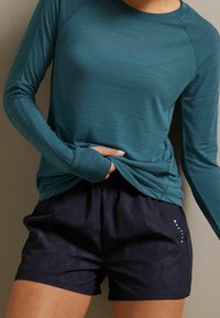 Teal Langarmshirt mit gerippter Textur, kombiniert mit schwarzen Sportshorts, die ein dezentes Muster und weißen "ACTIVE"-Text an der Seite aufweisen.