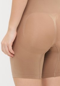 Shorts sagomati di colore marrone chiaro, realizzati in un tessuto morbido e elasticizzato. Presentano un design senza cuciture con bordi morbidi e una cintura elastica.