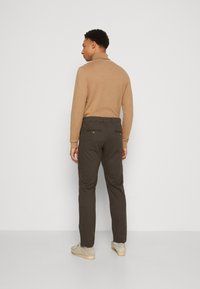 Brown long-sleeve shirt with a collar, paired with dark brown pants, featuring back pockets and beige suede shoes. Simple, minimalist design.