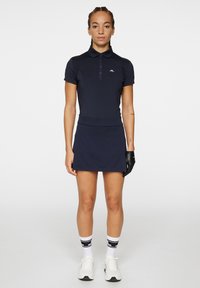 Marinblå kortärmad polo skjorta med krage och knappslån; matchande marinblå kjol; svart handske; vita strumpor med svarta ränder; vita sneakers.