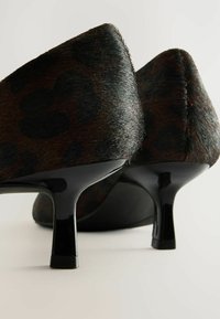 Chaussures à talons noires avec une texture imprimée léopard, présentant un talon noir brillant et un design de bout effilé. Coutures transparentes sur les bords.