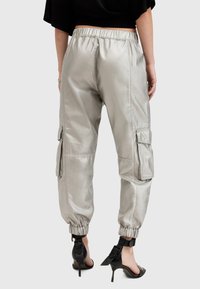 Srebrne metaliczne spodnie cargo z elastycznym paskiem w talii, mankietami na kostkach i bocznymi kieszeniami. Gładka tekstura z refleksyjnym wykończeniem.