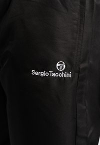 Zwarte jas met een gestructureerde afwerking. Bevat een opvallend wit geborduurd logo van "Sergio Tacchini" aan de linkerkant.