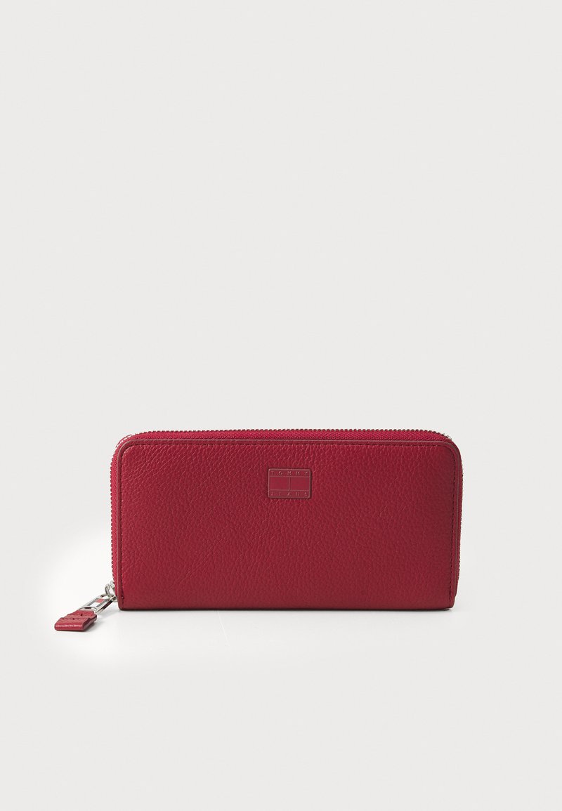 Portefeuille en cuir texturé rouge avec une fermeture éclair, de forme rectangulaire, et un petit accent en métal griffé à l'avant.