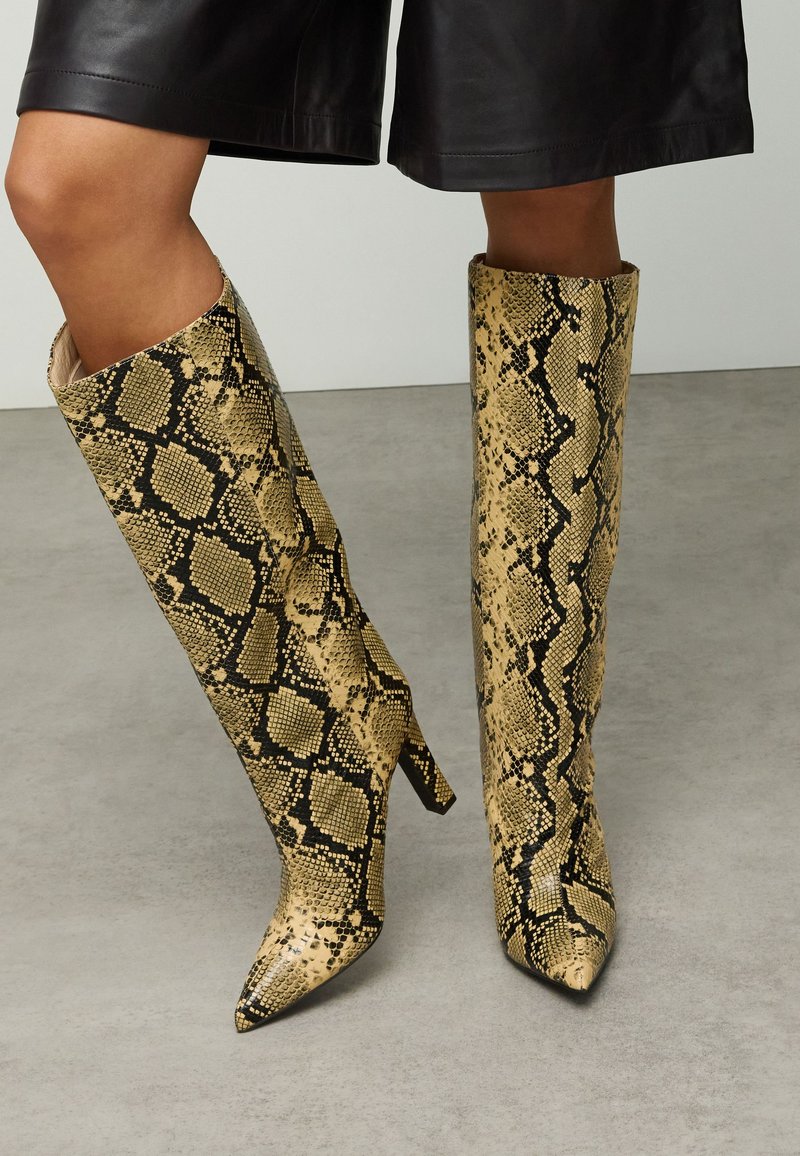 Knielange stiletto laarzen met een gestructureerd geel-zwart slangenprintontwerp, voorzien van een spitse neus en een nauwsluitend silhouet.