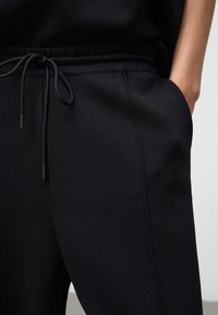 Zwarte joggingsbroek met een gestructureerde stof, een elastische tailleband met een trekkoord en zijzakken. Eenvoudig, functioneel ontwerp.