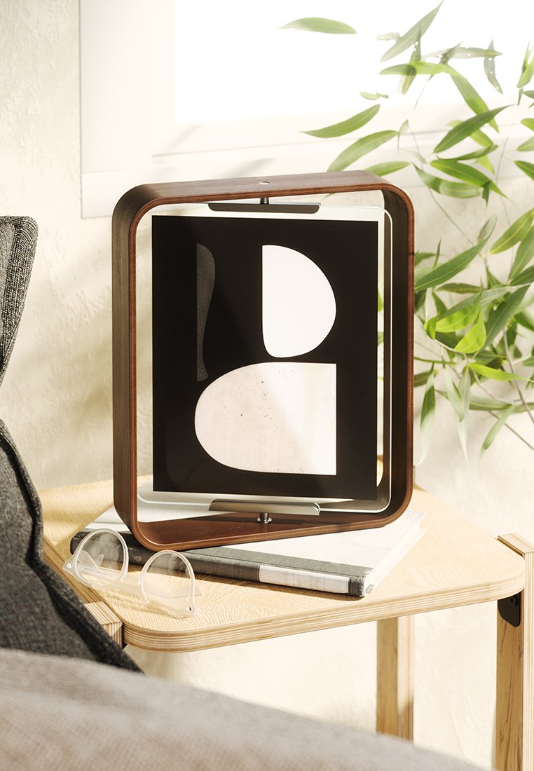 Drewniana ramka na zdjęcia w prostokątnym kształcie, prezentująca geometryczną czarno-białą grafikę. Przezroczysty szklany przód, ustawiona na jasnym drewnianym stole z okularami.