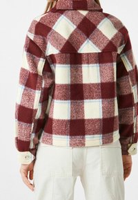 Rutig jacka med krage i vinröd, krämfärgad och ljusblå. Tillverkad av mjuk ullblandning med knappmanschetter och en detalj på ryggdetaljen.