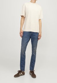 Camiseta de algodón beige de mangas cortas, combinada con jeans de mezclilla azul y zapatillas marrones con rayas blancas. Ajuste simple y relajado.