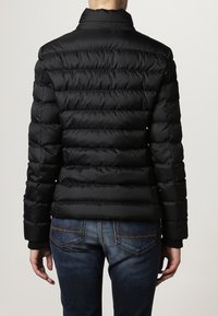 Black, quilted puffer jacket with a high collar and horizontal stitching, featuring a smooth, shiny texture. Worn over blue jeans.