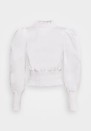 Haut en satin blanc avec un col haut froncé, des manches bouffantes et une taille élastiquée, présentant une texture lisse et polie.