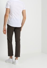 Vit kortärmad skjorta med rundad nederkant, kombinerad med mörkbruna byxor och vita sneakers, vilket framhäver en avslappnad, tät passform.