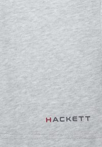 Camiseta de algodón gris con una textura suave y cuello redondo. El logo "HACKETT" está impreso en gris oscuro con un acento rojo.