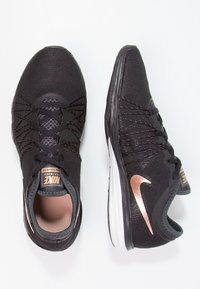 Mustat Nike-urheilukengät, joissa on verkkomateriaali yläosassa, hienovaraiset ruusukultaiset yksityiskohdat ja valkoinen pohja. Ominaisuuksiin sisältyvät teksturoidut nauhat ja pehmustettu nilkkasauma.