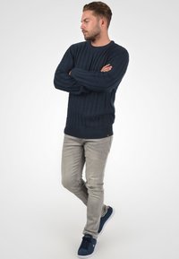 Pull en maille bleu marine avec un motif de côtes texturé, col rond et manches longues, associé à un jean gris clair et des baskets en suede bleu marine.