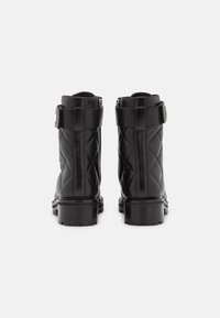 Botas de tobillo de cuero negro acolchado con suela gruesa, que presentan un detalle de correa y hebilla en el tobillo para mayor estabilidad y estilo.