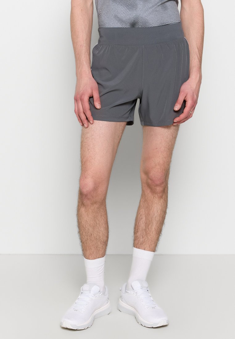 Pantaloni corti atletici grigi realizzati in tessuto leggero, con una vita elastica e un taglio corto, abbinati a scarpe sportive bianche e calze.