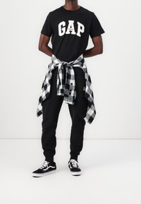 Černé bavlněné tričko s bílým logem "GAP", v kombinaci s černými tepláky a zavázanou černobílou kostičkovanou flanelovou košilí. Černé tenisky.