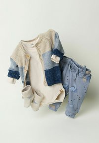 Strickjacke in Beige und Blau, Langarm-Body, blaue Hose mit Dinosauriermuster und helle Socken.