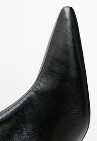 Black faux leather high-heeled shoe with a pointed toe design, featuring a smooth texture and a sleek silhouette.
