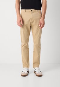 Beige chino's gemaakt van een katoenen mix, met een slim fit, voorzakken en een knoopsluiting. Gecombineerd met witte sneakers.