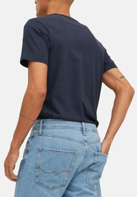 Marineblå bomulds T-shirt med korte ærmer og rund halsudskæring, brugt sammen med højtaljede lyseblå denim jeans med baglommer.