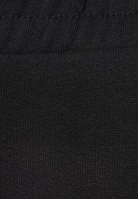 Schwarzer gestrickter Stoff mit glatter Textur, der ein geripptes Muster und gleichmäßige Nähte über die Oberfläche aufweist.