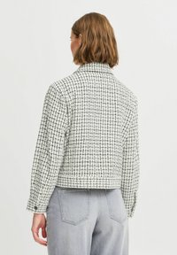 Vævet jakke i et sort-hvidt mønster, med krave og knapmanchetter. Den har et cropped design og er placeret på en lys baggrund.