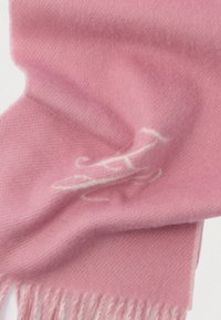 Mīksts rozā vilnas šalle ar baltu izšūtu ķirzaku dizainu un franjām, izvietota uz gaiša fona.