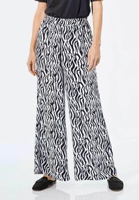 Wijduitlopende broek in zwart-wit zebra print, met een elastische tailleband en lichte stof. Gecombineerd met zwarte instapschoenen.