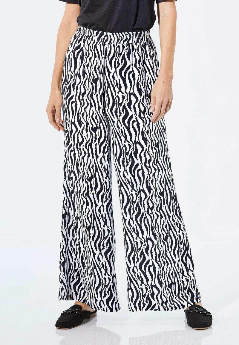 Wijduitlopende broek in zwart-wit zebra print, met een elastische tailleband en lichte stof. Gecombineerd met zwarte instapschoenen.