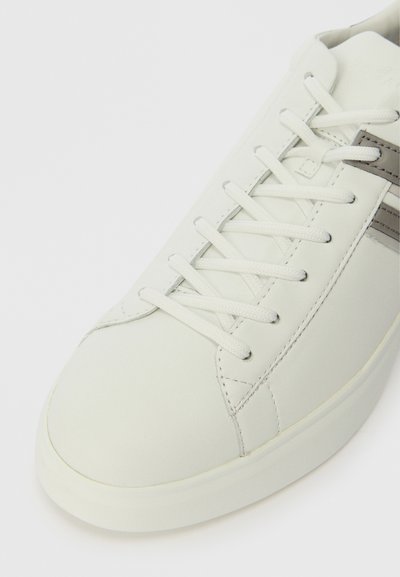 Baltie ādas sporta kurpes ar noapaļotu purngalu, plakanu šņorēm un pelēku svītru akcentu. Gluda tekstūra un minimālisma dizains.