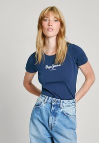 T-shirt bleu marine à manches courtes avec le logo blanc "Pepe Jeans London", associé à un jean en denim taille haute de couleur clair.