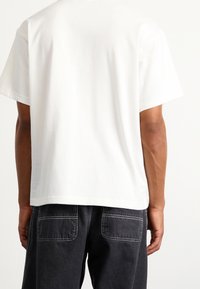 White cotton t-shirt with a relaxed fit, short sleeves, and a crew neckline, paired with black denim pants featuring back pockets.