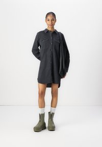 Black denim shirt dress with button front and two chest pockets. Paired with olive green ankle boots and light grey socks. Simple, tailored design.