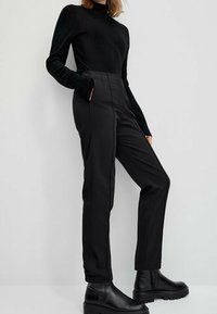 Black fitted trousers with a high waist, pockets, and side seams. Paired with a black long-sleeve top and black ankle boots. Smooth texture.