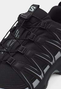 Μαύρο παπούτσι για τρέξιμο σε μονοπάτια με σύστημα γρήγορου δέσιμου, ανθεκτικές ενισχύσεις και επάνω μέρος από υφή διχτυού σχεδιασμένο για υπαίθρια αθλήματα.