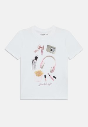 Vit bomull t-shirt med ett grafiskt tryck av en kamera, hörlurar, mobiltelefon, läppstift, pomfriter och en rosa rosett, märkt "Bara tjejgrejer."