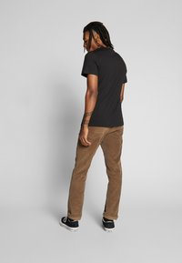 Black short-sleeve t-shirt and brown corduroy pants with rolled cuffs, worn with black sneakers. Subject is viewed from the back.