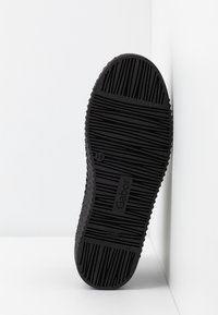 Semelle de chaussure en caoutchouc noir avec rainures verticales et horizontales, logo "Gabor" et taille 4½ indiquée, inclinée contre un coin blanc.