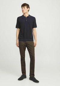 Polo shirt navy a maniche corte realizzato in tessuto testurizzato, con colletto e pianetta a tre bottoni. Abbinato a pantaloni marroni e scarpe nere.