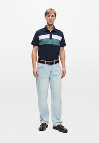 Laivastonsininen polo-paita, jossa on valkoisia ja turkooseja raitoja, lyhyet hihat, yhdistettynä vaaleansiinisiin farkkuihin ja ruskeisiin nahkakenkiin. Silkkinen kangas, rento leikkaus.