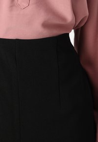 Černá sukně s hladkým povrchem a přiléhavým střihem, se rovnými liniemi a jemnými švy. Spárováno s světlou růžovou košilí.