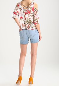 Blommig blus med kalla axlar och korta ärmar, tillverkad av mjukt material och med korsade band på baksidan. Matchas med ljusblå denimshorts och gula klackar.