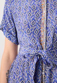 Vestido azul de mangas curtas com um padrão de folhas em creme e azul-marinho, com um cinto na cintura e detalhes em botão na frente.