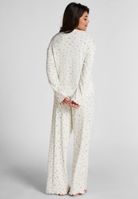 Lange mouwen, geribbelde pyjama set in crème met groene bloemenpatronen. Ontspannen pasvorm met uitlopende broekspijpen en geschulpte manchetten bij de mouwen en de zoom.