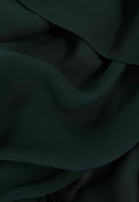 Dunkelgrüner Stoff mit einer weichen, strukturierten Oberfläche, die sanfte Falten und Wellen zeigt und seinen fließenden Fall sowie nahtlose Kanten betont.