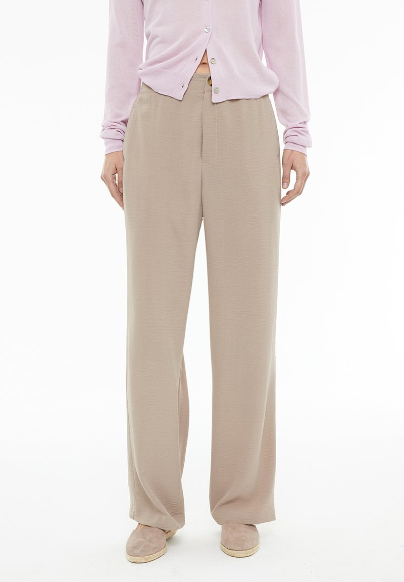Beige wide-leg trousers made of soft fabric, featuring a flat front, high waist, and a smooth texture; paired with a light pink cardigan.