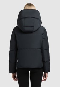 Svart dunjacka med en stor huva, med quiltat mönster och sidoliknande logotypdetalj. Slät textur, kort längd och långa ärmar.